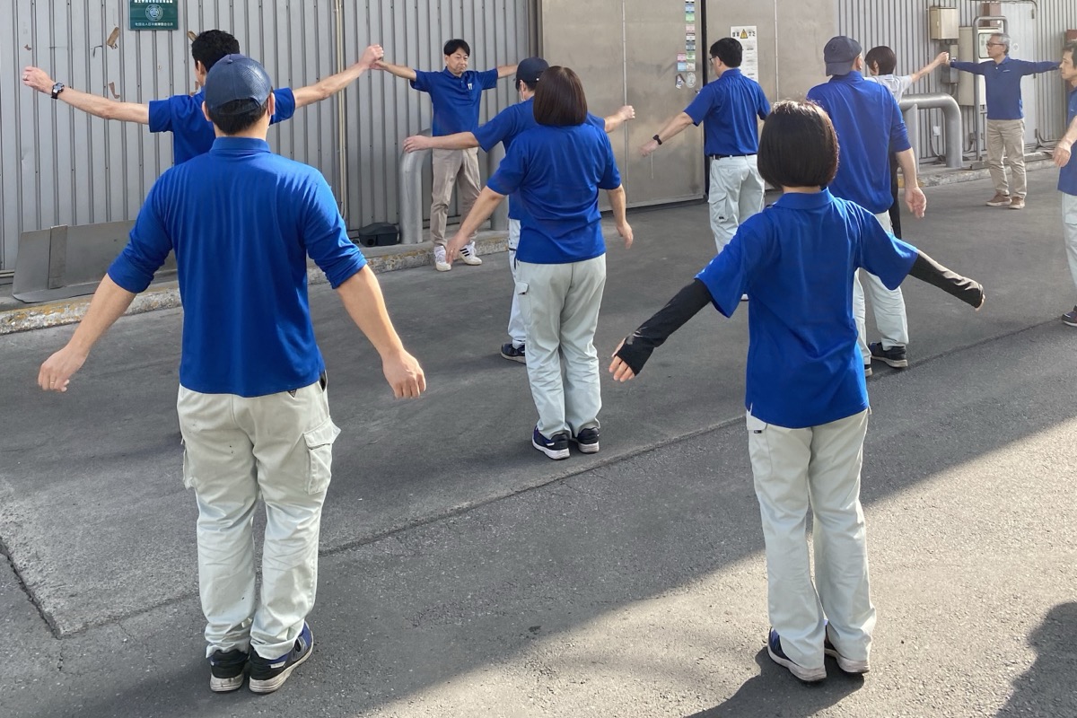 屋外で輪になってラジオ体操をする従業員
